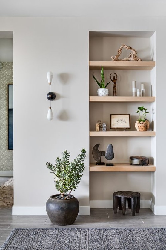an awkward nook turned into a display with a series of niche shelves, some decor and potted plants, a black stool and a potted plant