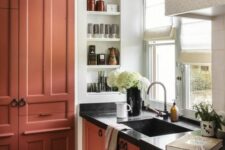 45 a terracotta kitchen with shaker cabinets and black countertops, a niche with shelves used for spaces and decor