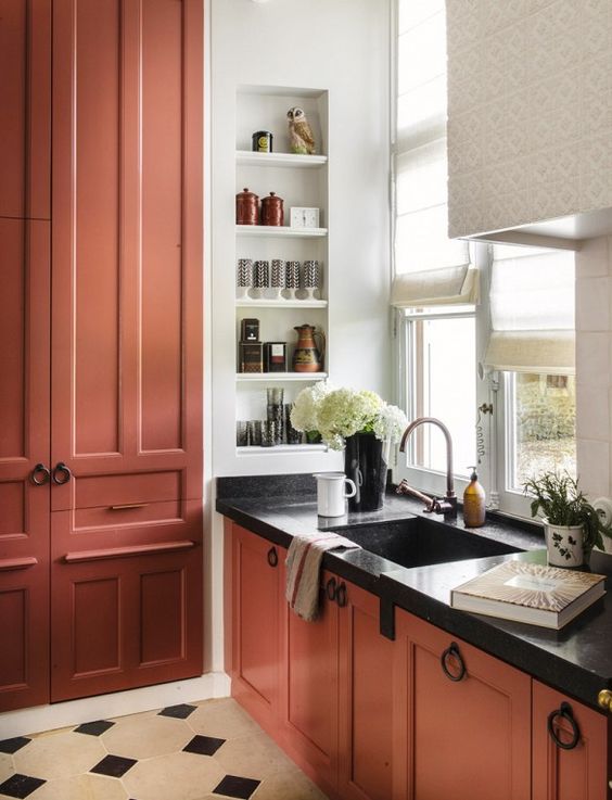 a terracotta kitchen with shaker cabinets and black countertops, a niche with shelves used for spaces and decor