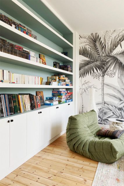 a reading nook with built-in niche shelves done green, with cabinets, a green chair, a wall mural and a boho rug is a welcoming space