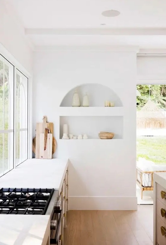 an airy white kitchen with an arched niche with beautiful tableware on display is a chic and lovely space