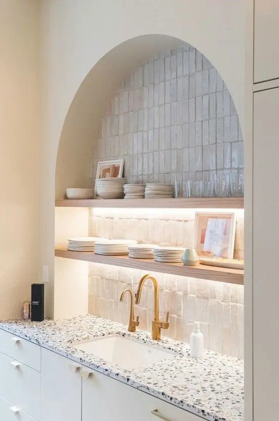 an arched niche clad with skinny tiles, open lit up shelves, porcelain and glasses is a decorative and practical idea for a kitchen