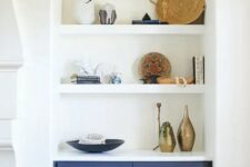 59 an arched niche with shelves that shows off stacks of books, baskets, vases and dishes plus a navy built-in cabinet for storage