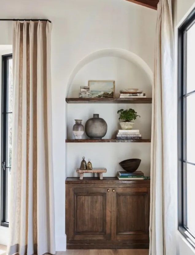 an awkward nook turned into a catchy part of decor, with an arched niche, a dark-stained cabinet and shelves, with some decor on display