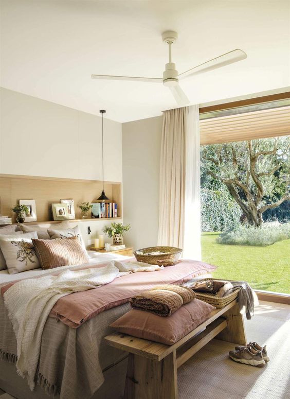 a Provence bedroom with a bed with neutral bedding, a bench with pillows, a glazed wall and a niche used for storage