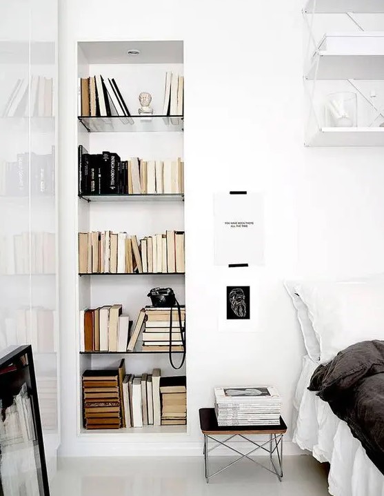 a Scandinavian bedroom with a bed and black and white bedding, a nightstand, a niche with bookshelves, some artwork