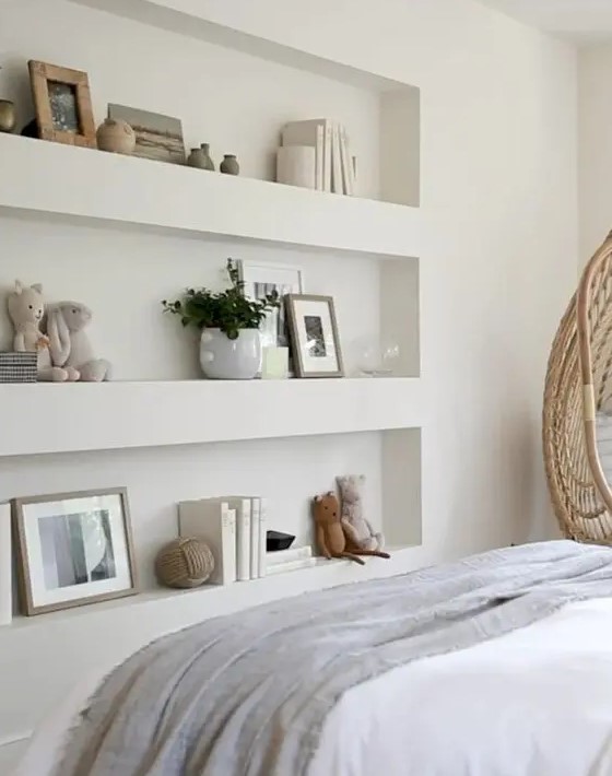 a Scandinavian bedroom with a series of niches with decor and books, a bed with neutral bedding and an egg-shaped chair