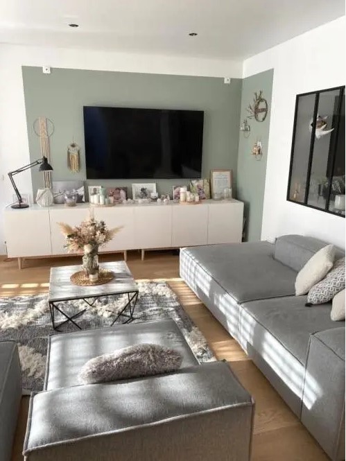 a Scandinavian living room with a green accent wall, a TV unit with decor, a low grey sofas and loungers, a coffee table