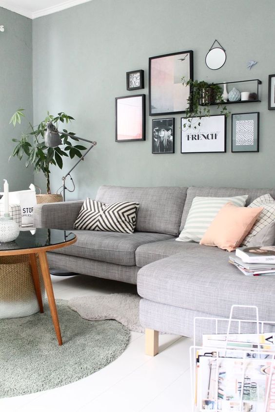 a Scandinavian living room with olive green walls, a grey sectional, a coffee table, a gallery wall and some greenery