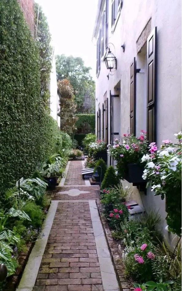a beautiful and elegant floral walkway with a brick path, a living wall and lots of greenery and blooms around