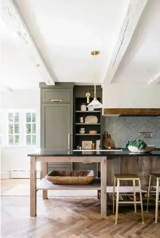 a beautiful farmhouse kitchen with an olive green cabinet and a stained kitchen island, a hood, pendant lamps and gold and brass knobs