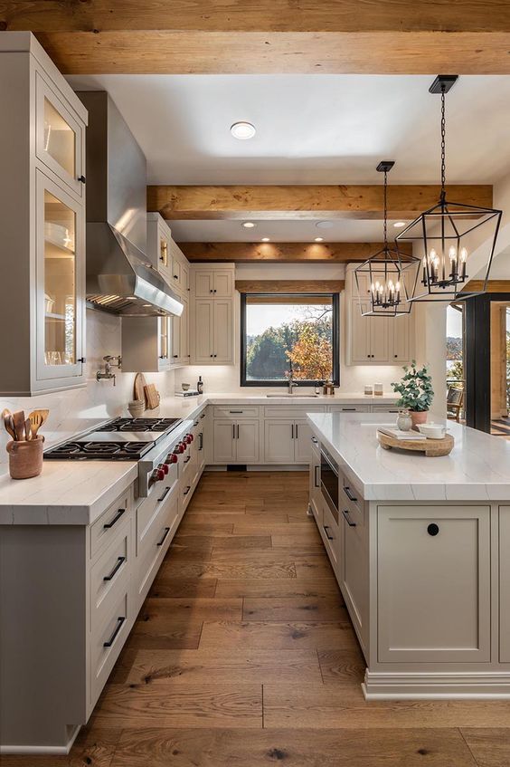 a beautiful modern farmhouse kitchen with dove grey cabinets, white stone countertops, wooden beams, pendant lamps