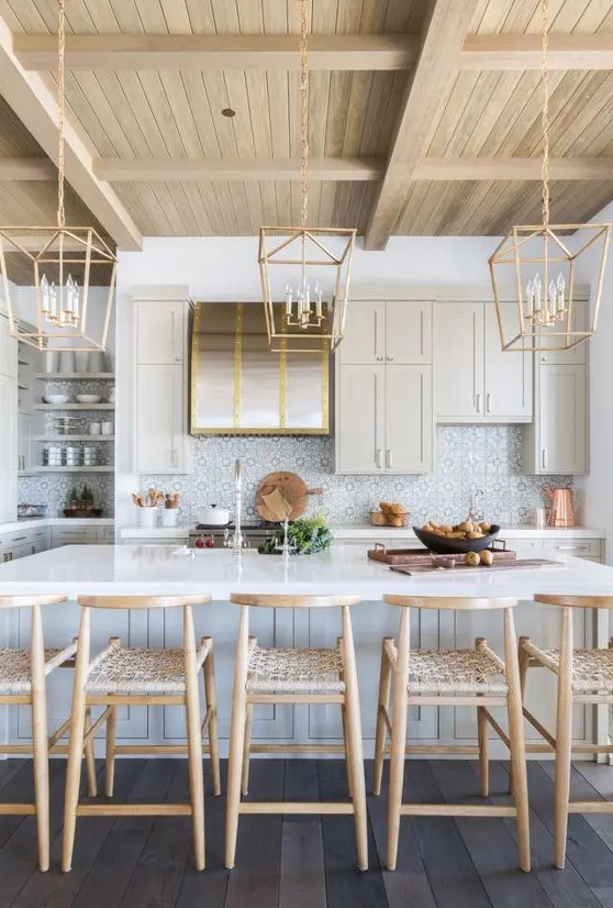 a beautiful modern farmhouse kitchen with tan cabinets, a kitchen island, a printed tile backsplash, woven stools and pendant lamps