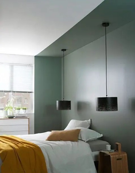 a bedroom with a large green niche where the bed is placed, a dresser, a stool and black pendant lamps is welcoming and cool