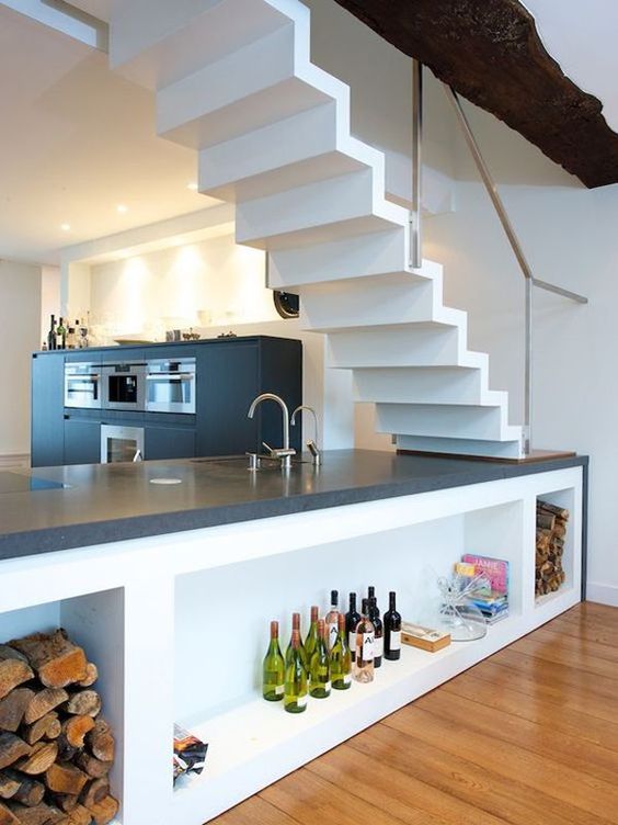 a black modern kitchen with a kitchen island placed under the stairs, with storage compartments and lights