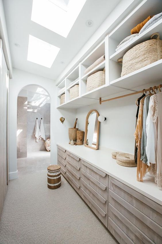 a boho attic closet with open storage compartments and baskets, dressers, an arched mirror, railing with clothes and a stool