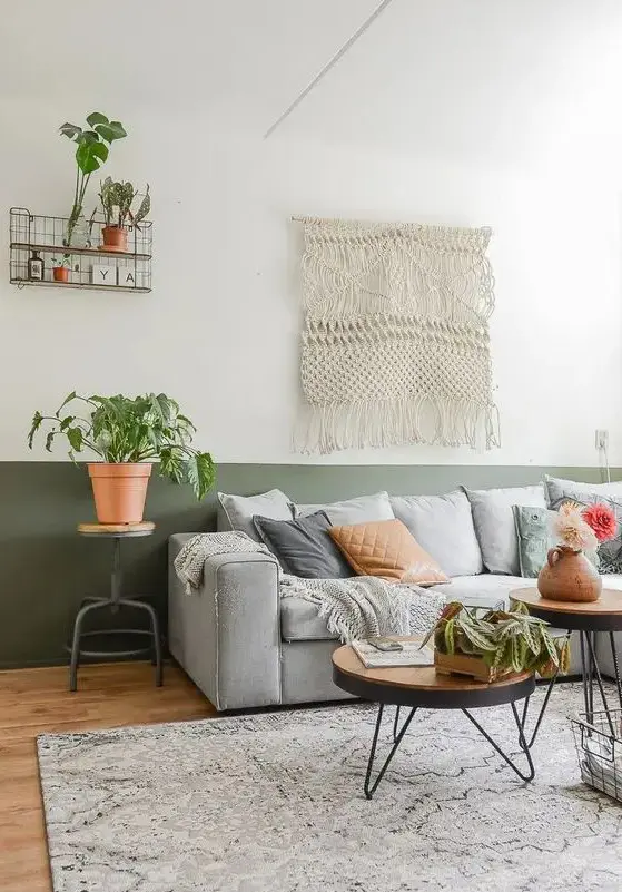 a boho living room with a color block accent wall in green and white, with a light grey sofa with pillows, a macrame, potted greenery