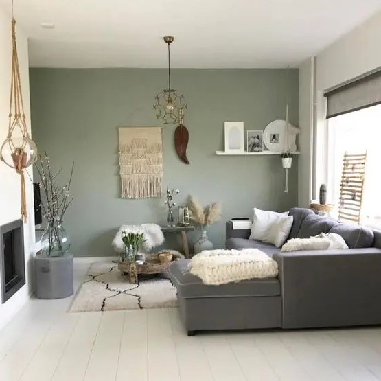 a boho living room with a green accent wall, a grey sectional, a built-in fireplace, a lot of cool and catchy boho home decor