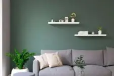 a bold living room with a dark green accent wall, a grey sofa, a couple of edges, poufs, potted greenery and a white coffee table