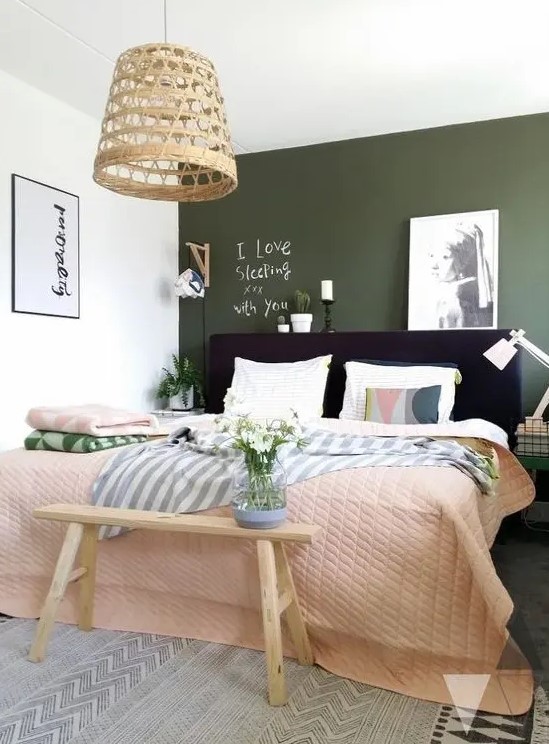 a bright bedroom with an olive green accent wall, a black upholstered bed with bright bedding, a bench and some lamps