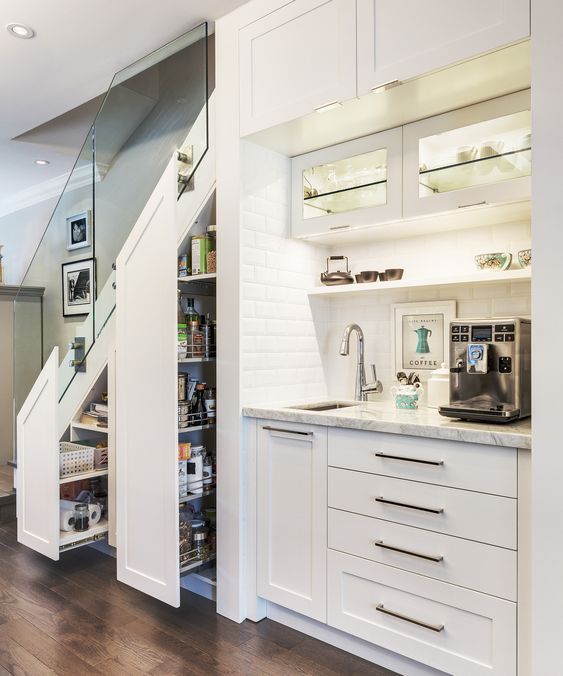 a built-in kitchen under the stairs with lights, tall drawers to store food and other stuff as in a pantry