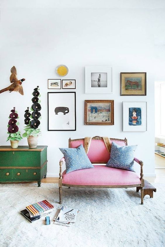 a catchy and bright space with a pink loveseat, a green sideboard, a free form gallery wall and some pretty decor
