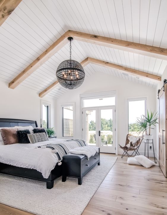 a catchy modern farmhouse bedroom with a shiplap ceilign, a black bed with contrasting bedding, a black dresser and a sphere lamp