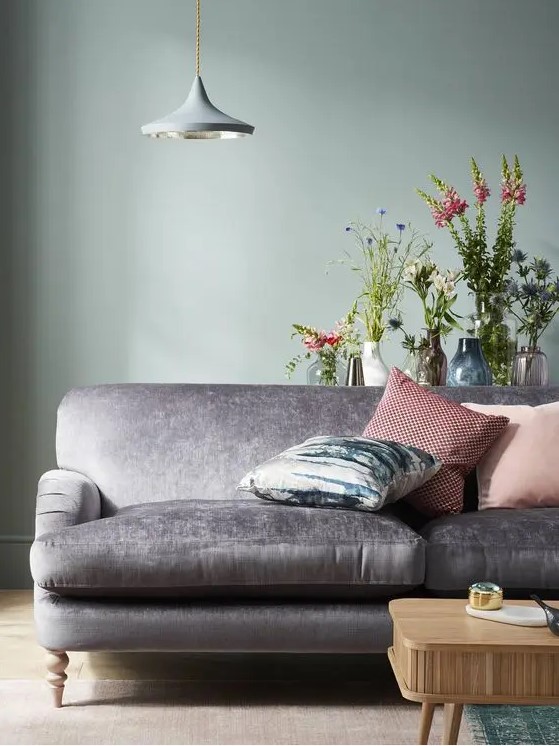 a catchy space with a pale green accent wall, a grey sofa with pillows, a wooden coffee tables and some blooms