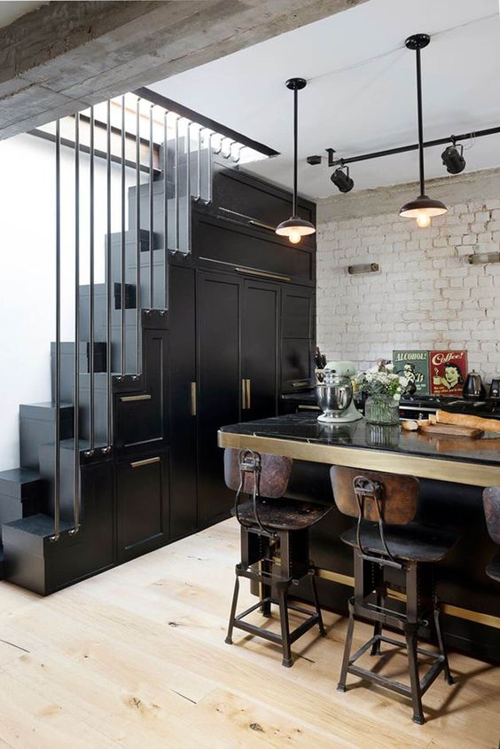 a catchy vintage kitchen in black with cabinetry built into the staircase, a large table that is a kitchen island and vintage decor