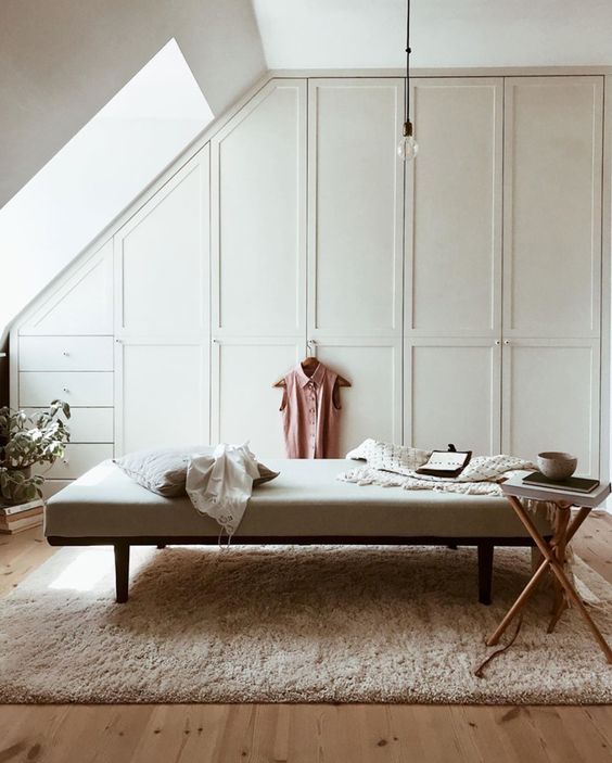 a chic attic closet with built-in wardrobes, a dressers, a large upholstered bench, a fluffy rug, a side table