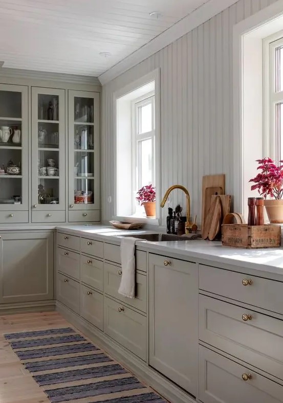a chic kitchen with grey shaker cabinets and glass ones, a white beadboard backsplash, a white stone countertop