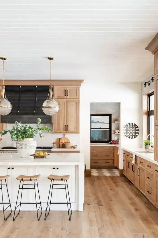 a chic modern country kitchen with light stained cabinets and hardwood floors, a white kitchen island, tall stools and pendant lamps
