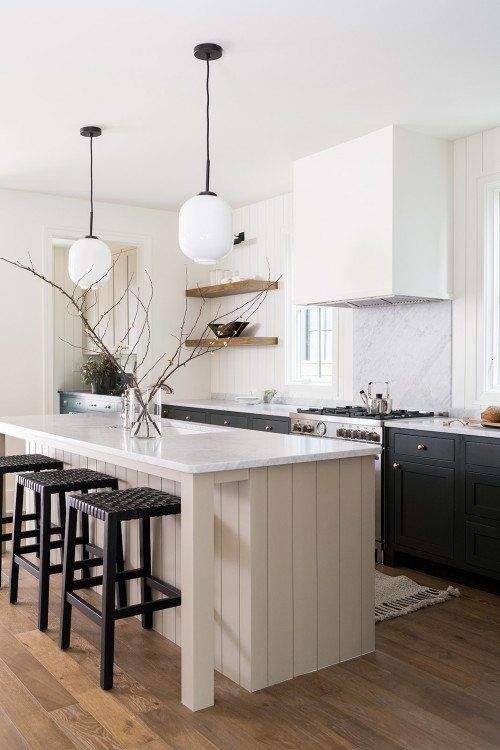a chic modern farmhouse kitchen with black cabinets, a shiplap tan kitchen island, black stools and pendant lamps