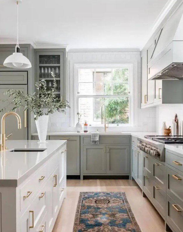 a classic sage green kitchen with shaker and glass front cabinets, a white stone countertop and square tiles, a creamy kitchen island
