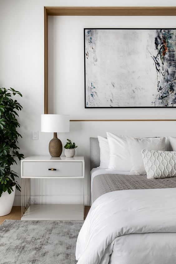 a contemporary bedroom with a niche to accent an artwork, a bed with neutral bedding, a creative nightstand and grenery