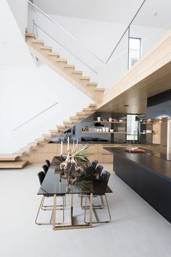 a contemporary kitchen placed under the staircase, with a mirror backsplash, open shelves and a black kitchen that doubles as a bar