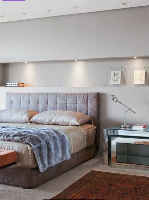 a contemporary luxurious bedroom with a lit up niche with decor, a leather bed with neutral bedding, mirror nightstands and rugs