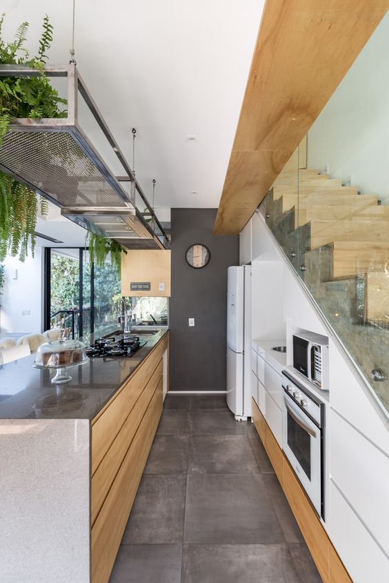 a contemporary white kitchen with sleek built-in storage units in the staircase, a large kitchen island, a metal shelf with greenery