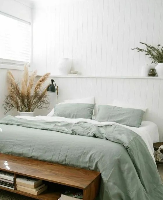 a cool bedroom with white shiplap walls, a bed with green and white bedding, a stained bench and black sconces