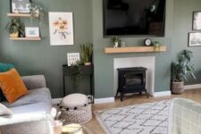 a cool green living room with a hearth, some shelves, a TV, a grey sofa with pillows, a a rug and some lovely and cool decor