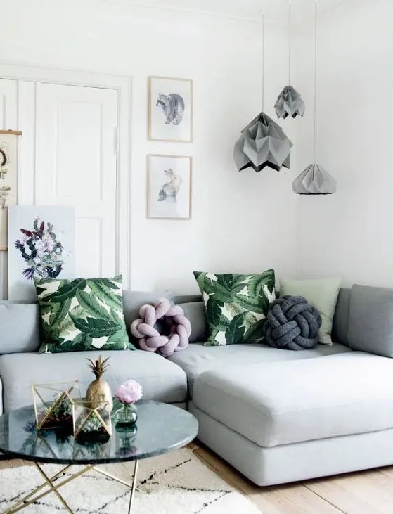 a cool living room with a light grey sectional, grey architecural lamps, bold green pillows and a gallery wall