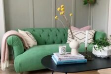 a cool living room with grey paneling, a bold green sofa with graphic pillows, a tiered coffee table and some plants
