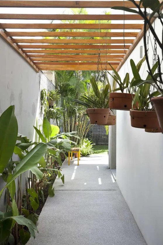 a covered side yard with a stone path, some tropical greenery along it and some greenery in hanging planters