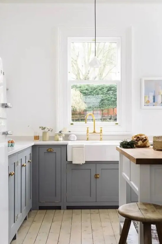 a cozy farmhouse kitchen with grey shaker cabinets, white countertops, a white kitchen island with a butcherblock countertop and pendant lamps