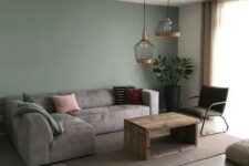 a cozy living room with a green accent wall, a low grey sofa, a stained coffee table, a dark green chair and a couple of pendant lamps