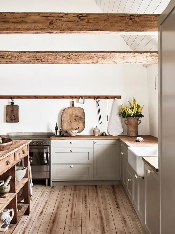 a cozy modern farmhouse kitchen with dove grey cabinets, stained countertops and wooden beams, a stained kitchen island and a stained floor
