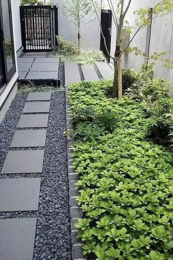 a dreamy modern side yard with pebbles and stone tiles, with flower beds with greenery and trees is a chic space with a touch of Zen