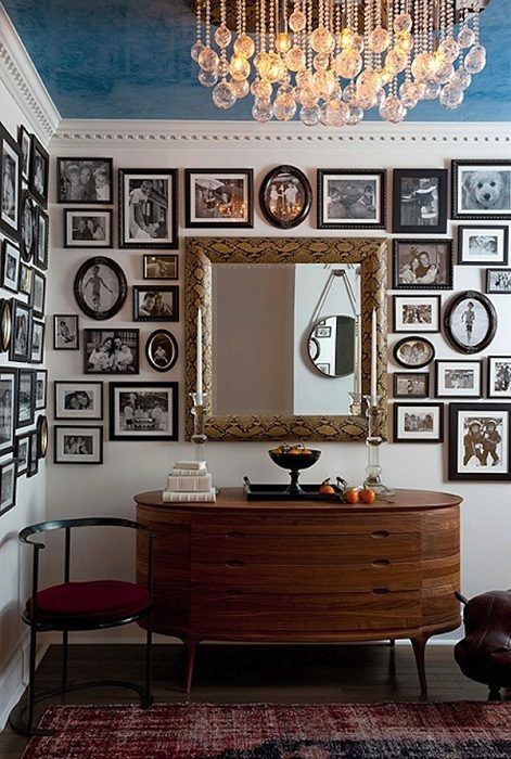 a fantastic vintage space with a rounded credenza, a printed rug and a rounded chair, a mirror and a free form black and white gallery wall that takes several walls