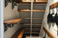 a farmhouse stairs pantry with open shelves with wrought details, wooden rails with hooks and built-in stained shelves and wine bottle stands