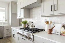 a grey farmhouse kitchen with shaker style cabinets, a white tile backsplash and white countertops plus black fixtures